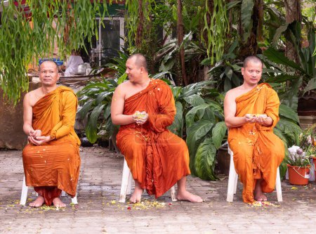 Photo for Ban Chang, Thailand - April 16, 2023: 3 monks wet from having water with flower petals over themselves during celebration of Songkran, Buddhist New Year, at Wat Chak Mak in Ban Chang, Rayong Province, Thailand. - Royalty Free Image