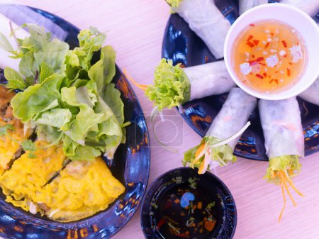 Photo for Two Vietnamese dishes, banh xeo and goi cuon (spring rolls) with condiments at a restaurant in Thanh Hoa, Vietnam. Shallow depth of field with the spring rolls and the salad in focus. - Royalty Free Image