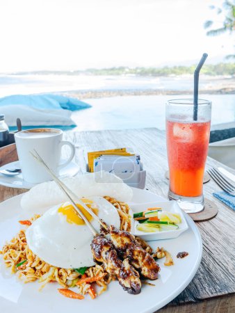 Téléchargez les photos : Mie goreng (nouilles frites) servi avec deux bâtonnets de satay de poulet et un œuf frit dans un restaurant sur la plage Medewi à Bali, Indonésie. - en image libre de droit