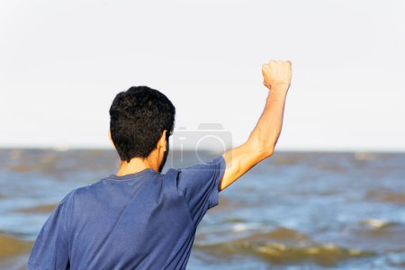 Foto de Un hombre levantando su brazo victorioso frente al río - Imagen libre de derechos