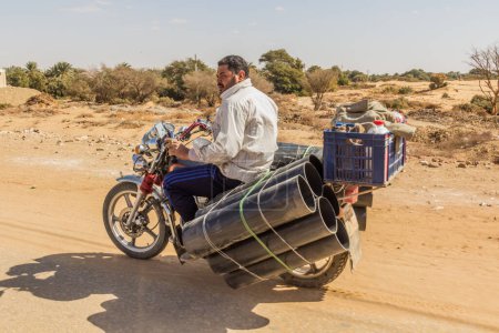 Foto de DAKHLA, EGYPT - FEBRUARY 8, 2019: Motorbike carrying thick pipes in Al Qasr village in Dakhla oasis, Egypt - Imagen libre de derechos