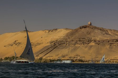Foto de ASWAN, EGYPT: FEB 15, 2019: Felucca sail boats under the Qubbet el-Hawa at the river Nile in Aswan, Egypt - Imagen libre de derechos