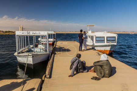 Foto de ASWAN, EGYPT - FEB 13, 2019: Pier near Kalabsha temple in the Nasser lake with the Aswan high dam in the background, Egypt - Imagen libre de derechos