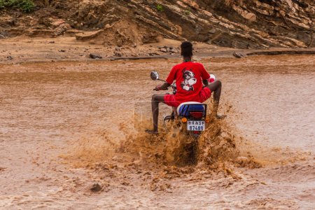 Photo for OMO VALLEY, ETHIOPIA - FEBRUARY 4, 2020: Local boy on a motorbike crossing swollen waters of Kizo river, Ethiopia - Royalty Free Image
