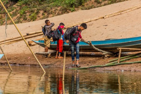 Photo for NAM OU, LAOS - NOVEMBER 24, 2019: Boys with a boat at Nam Ou river in Luang Prabang province, Laos - Royalty Free Image