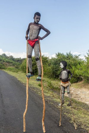 Foto de OMO VALLEY, ETIOPÍA - 5 DE FEBRERO DE 2020: Niños de la tribu Banna caminando sobre pilotes, Etiopía - Imagen libre de derechos