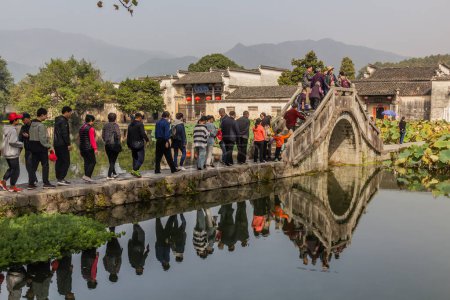 Foto de HONGCUN, CHINA - 29 DE OCTUBRE DE 2019: La gente cruza un puente sobre el lago Sur en la aldea de Hongcun, provincia de Anhui, China - Imagen libre de derechos