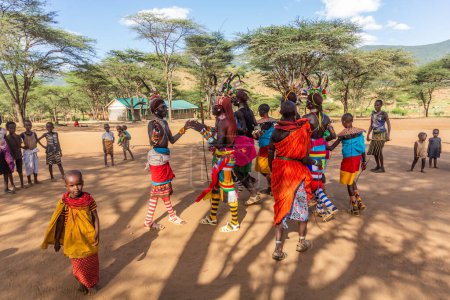 Foto de SUR HORR, KENIA - 12 DE FEBRERO DE 2020: Grupo de hombres y mujeres jóvenes de la tribu Samburu bailando con coloridos tocados hechos de plumas de avestruz después de la ceremonia de la circuncisión masculina. - Imagen libre de derechos