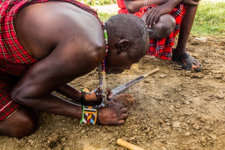 Foto de MASAI MARA, KENIA - 20 DE FEBRERO DE 2020: Masai hombres haciendo un fuego en su aldea, Kenia - Imagen libre de derechos
