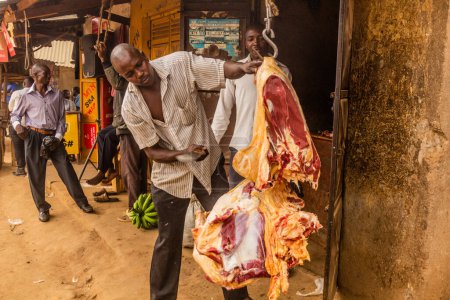 Photo for BUDADIRI, UGANDA - FEBRUARY 25, 2020: Local butcher cutting meat in Budadiri village, Uganda - Royalty Free Image