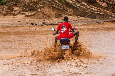Foto de OMO VALLEY, ETIOPÍA - 4 DE FEBRERO DE 2020: Niño local en una motocicleta cruzando aguas hinchadas del río Kizo, Etiopía - Imagen libre de derechos