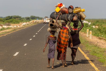 Photo for OMO VALLEY, ETHIOPIA - FEBRUARY 5, 2020: Tribal women carrying loads on their heads on a road between Turmi and Omorate in Omo valley, Ethiopia - Royalty Free Image