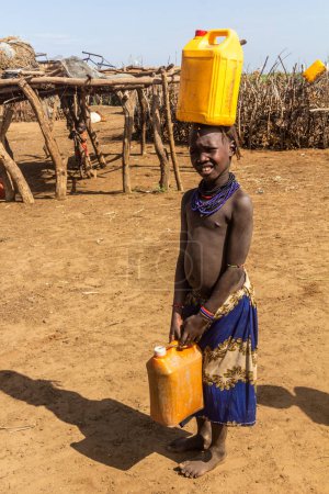 Photo for OMORATE, ETHIOPIA - FEBRUARY 5, 2020: Daasanach tribe girl collecting water near Omorate, Ethiopia - Royalty Free Image