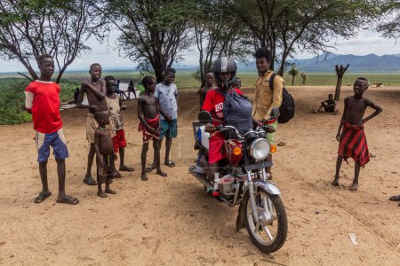 Téléchargez les photos : KORCHO, ÉTHIOPIE - 4 FÉVRIER 2020 : Des garçons de la tribu Karo dans leur village de Korcho avec des visiteurs extérieurs sur une moto, en Éthiopie - en image libre de droit