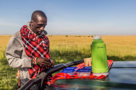 Foto de MASAI MARA, KENIA - 19 DE FEBRERO DE 2020: Guía local Masai que prepara un box lunch en la Reserva Nacional Masai Mara, Kenia - Imagen libre de derechos