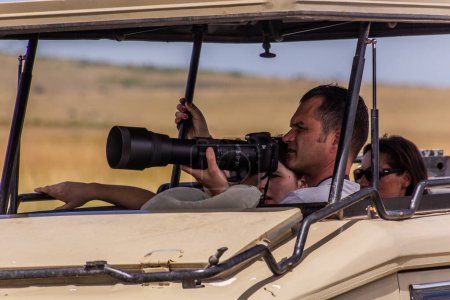 Photo for MASAI MARA, KENYA - FEBRUARY 19, 2020: Photographer in a safari vehicle in Masai Mara National Reserve, Kenya - Royalty Free Image