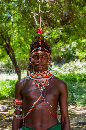 Photo for SOUTH HORR, KENYA - FEBRUARY 12, 2020: Samburu tribe young man wearing a colorful headpiece made of ostrich feathers after his circumcision ceremony. Taken in South Horr village, Kenya - Royalty Free Image