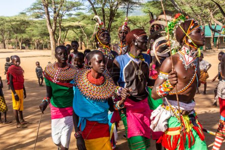 Foto de SUR HORR, KENIA - 12 DE FEBRERO DE 2020: Grupo de hombres y mujeres jóvenes de la tribu Samburu bailando con coloridos tocados hechos de plumas de avestruz después de la ceremonia de la circuncisión masculina. - Imagen libre de derechos