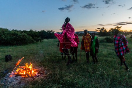 Foto de MASAI MARA, KENIA - 20 DE FEBRERO DE 2020: Masai hombres realizando su Baile de Salto junto a una hoguera, Kenia - Imagen libre de derechos