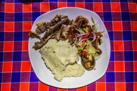 Foto de Comida preparada por Masai en Kenia - carne de cabra asada, salchichas, ensalada y ugali. - Imagen libre de derechos