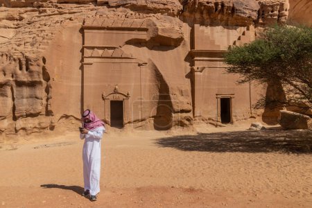 Téléchargez les photos : AL ULA, ARABIE SAOUDITE - 9 NOVEMBRE 2021 : Homme local à côté des tombes coupées 39 et 40 dans la colline Jabal Al Banat au site Hegra (Maca'in Salih) près d'Al Ula, en Arabie Saoudite - en image libre de droit