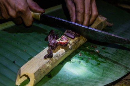 Téléchargez les photos : Guide local avec viande fumée sur un bambou dans la forêt près de Luang Namtha, Laos - en image libre de droit