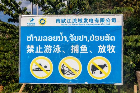 Photo for NAM OU, LAOS - NOVEMBER 23, 2019: Sign now swimming, no fishing, no cattle at the Nam Ou 5 dam, Laos - Royalty Free Image