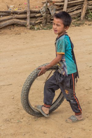 Foto de SAMARKISAY, LAOS - 22 de noviembre de 2019: Niño local jugando con un neumático en la aldea de Samarkisay en la provincia de Phongsali, Laos - Imagen libre de derechos