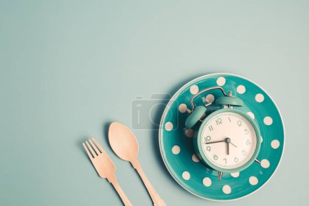 Téléchargez les photos : Un réveil sur une assiette vide et des couverts sur fond bleu pour le concept de nourriture, de gestion du temps, de perte de poids et de manger à temps. - en image libre de droit