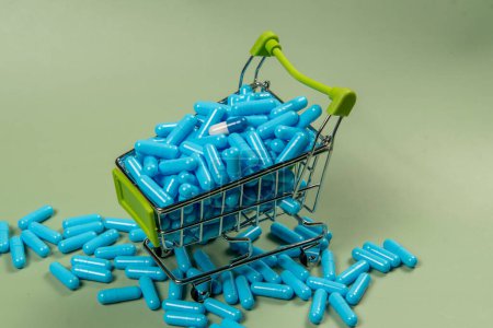 Blaue Pillen in einem Einkaufswagen auf grünem Hintergrund. Konzept zum Kauf von Medikamenten