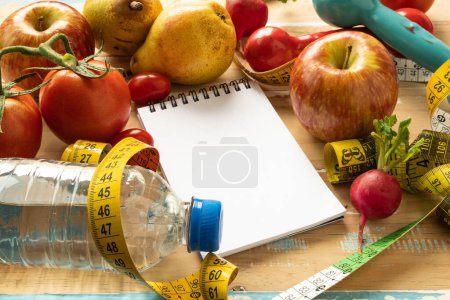 bloc de notas de papel con frutas y equipos de gimnasio asociados con la dieta y la pérdida de peso