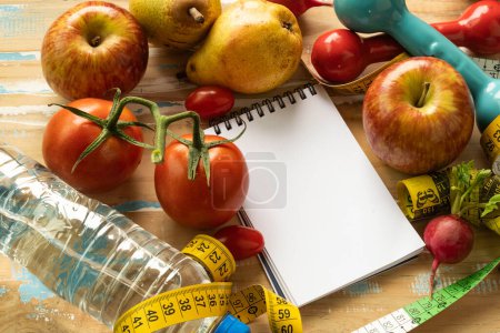 Papier-Notizblock mit Obst und Fitnessgeräten im Zusammenhang mit Ernährung und Gewichtsverlust