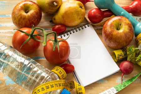 Papier-Notizblock mit Obst und Fitnessgeräten im Zusammenhang mit Ernährung und Gewichtsverlust