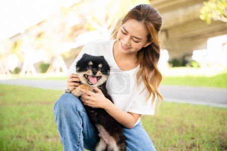 Téléchargez les photos : Happy young asian woman playing and sitting on grass in the park with her dog. Pet lover concept - en image libre de droit
