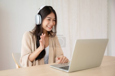 Téléchargez les photos : Jeune femme asiatique portant casque tout en travaillant sur ordinateur portable à la maison. Travail à domicile, vidéoconférence, vidéoconférence, cours en ligne sur l'apprentissage des élèves - en image libre de droit