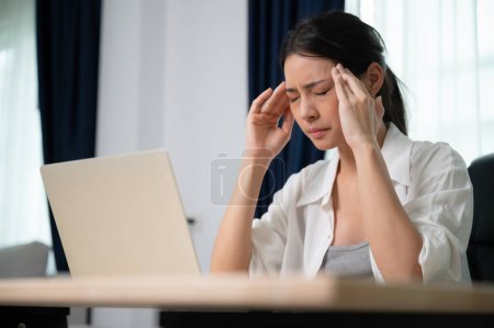 Foto de Síndrome de oficina. Sobretrabajado cansado joven asiática mujer sintiendo dolor de cabeza, teniendo problemas de vista después de ordenador portátil trabajo. Mujer joven estresada que sufre de fatiga en casa - Imagen libre de derechos