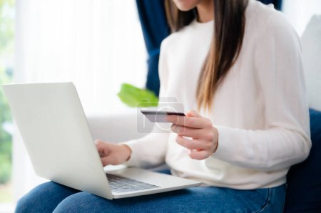 Photo for Young asian woman sitting on sofa in living room, makes online banking payments through the internet from bank card on computer laptop. Shopping online on notebook with credit card - Royalty Free Image