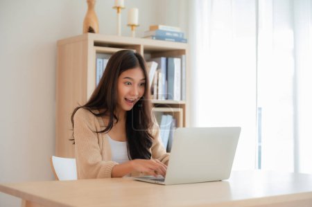 Photo for Happy euphoric young asian woman celebrating winning or getting ecommerce shopping offer on computer laptop. Excited happy girl winner looking at notebook celebrating success - Royalty Free Image