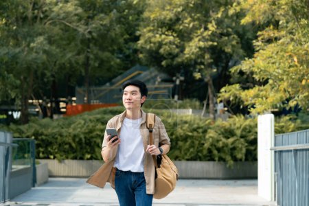 Photo for Portrait of handsome Asian student using smartphone. A young man walking outdoor happy smiling with holding mobile phone - Royalty Free Image