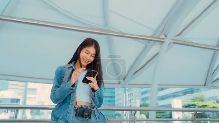 Photo for Young asian woman smiling using mobile smart phone outdoor. Happy female tourist wearing jeans jacket and holding smartphone at public - Royalty Free Image