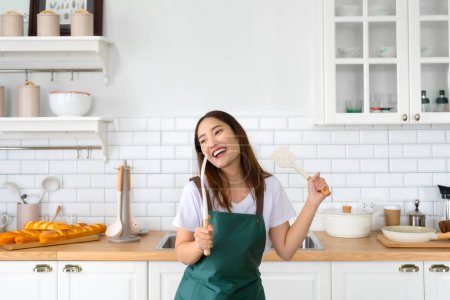 Photo for Young Asian woman dancing in the kitchen. The joy of a beautiful woman relaxing in her free time during the weekend in the house - Royalty Free Image