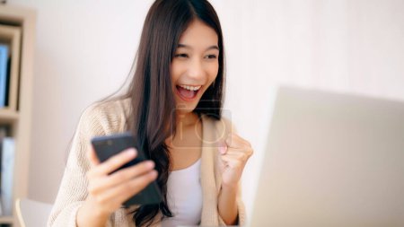 Photo for Young asian woman happy working on computer laptop and hand typing chat message on mobile smartphone at home. Video call, Online meeting - Royalty Free Image