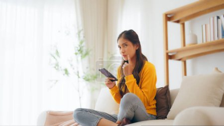 Photo for Happy young asian woman relax on comfortable couch at home, typing chat message on smartphone, smiling girl use cell phone chatting, searching information on browser wireless internet, online shopping - Royalty Free Image