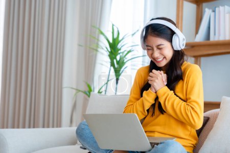 Photo for Young happy lucky woman student feeling excited winning, using computer laptop and sitting on sofa, adorable Asian female receiving great news on notebook, getting new job celebrating success - Royalty Free Image