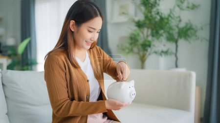 Photo for Young Asian woman putting coin in piggy bank. Save money and financial investment - Royalty Free Image