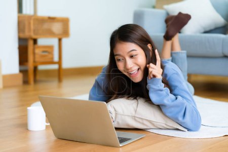 Photo for Young asian woman smile working in living room at home. Happy female using computer laptop and lying on the floor at house, Video call with friend - Royalty Free Image