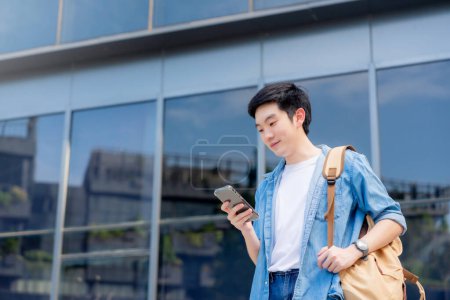 Photo for Portrait of handsome Asian student using smartphone. A young man standing outdoor happy smiling with holding mobile phone - Royalty Free Image