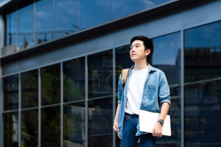 Photo for Portrait of handsome Asian student holding computer laptop and backpack. A young man standing outdoor happy smiling - Royalty Free Image