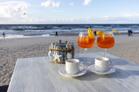 Photo for Beach cafe, two cups of coffee and drinks on the table. In the background the Baltic Sea and an empty beach off the season, Island Wolin, Miedzyzdroje, Poland - Royalty Free Image