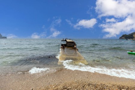 Foto de Budva, Montenegro - 28 de junio de 2023: Muelle de piedra en la playa con Ricardova Glava Beach junto al mar Adriático junto a City Walls - Imagen libre de derechos